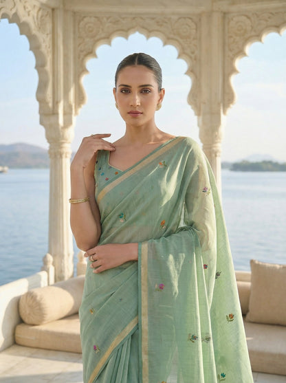 Woman in a light green saree standing in front of an architectural structure with a scenic background. Pista Green Jamdani Cotton Saree