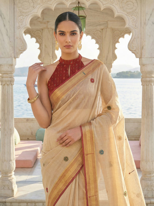 Woman in a traditional beige saree with a red blouse, standing in an architectural setting with a scenic background. Cream Banarasi Style Jamdani Cotton Saree for women