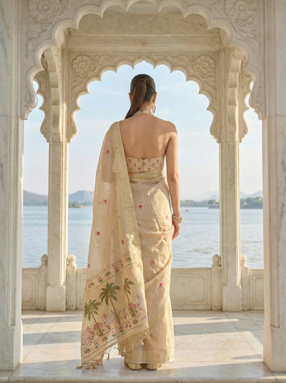 Woman in a beige saree with floral patterns standing in an architectural setting overlooking water. Off White Pichwai Jamdani Cotton Saree | Pichwai sarees